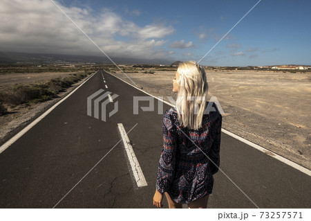Blonde long hair girl viewed fromback walk on a long straight asphalt road - concept of freedom and independence - hope and future for next destination in life Blonde long hair girl viewed fromback walk on a long straight asphalt road - concept of freedom and independence - hope and future for next destination in life 73257571