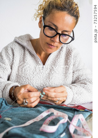 Portrait of middle age caucasian woman working at home tailoring with clothes to repair or hand made - tailor job with independent people in home work leisure activity Portrait of middle age caucasian woman working at home tailoring with clothes to repair or hand made - tailor job with independent people in home work leisure activity 73257594