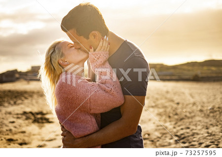 Kiss and love couple outdoor with two young man and woman kissing and hugging in a golden sunset background - people enjoy together forever life - concept of different ages male female Kiss and love couple outdoor with two young man and woman kissing and hugging in a golden sunset background - people enjoy together forever life - concept of different ages male female 73257595