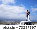 Love and travel people lifestyle - standing couple on the roof vehicle van together kissing and hugging with long road and blue sky in background for destination concept.- free lifestyle and 73257597