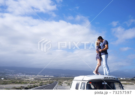 Love and travel people lifestyle - standing couple on the roof vehicle van together kissing and hugging with long road and blue sky in background for destination concept.- free lifestyle and Love and travel people lifestyle - standing couple on the roof vehicle van together kissing and hugging with long road and blue sky in background for destination concept.- free lifestyle and 73257597