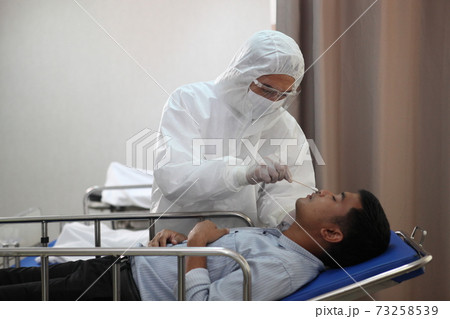 Doctors in full protective gear collects a sample from a mature man on bed as part of the operations of a coronavirus mobile testing unit. Doctors in full protective gear collects a sample from a mature man on bed as part of the operations of a coronavirus mobile testing unit. 73258539