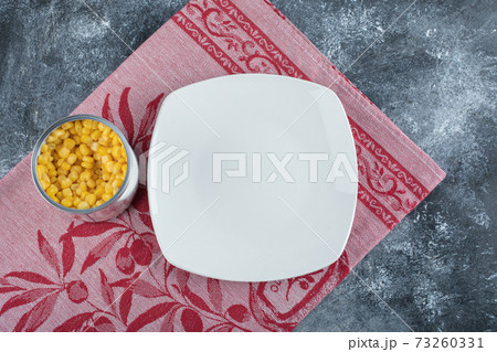 A can full of popcorn seeds with empty plate on a tablecloth 73260331