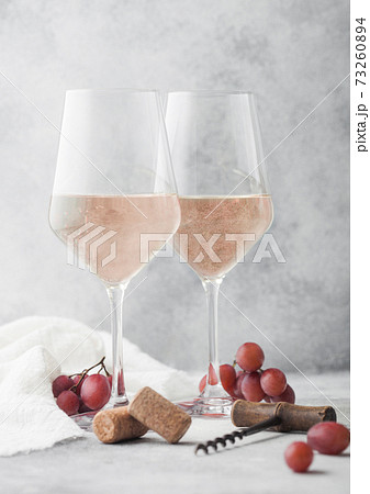 Glasses of rose pink summer wine with corks, grapes and corkscrew on light background. 73260894