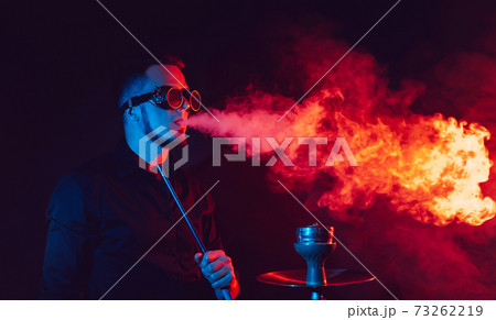 man in futuristic glasses smokes a hookah and blows a cloud of smoke in a shisha bar 73262219