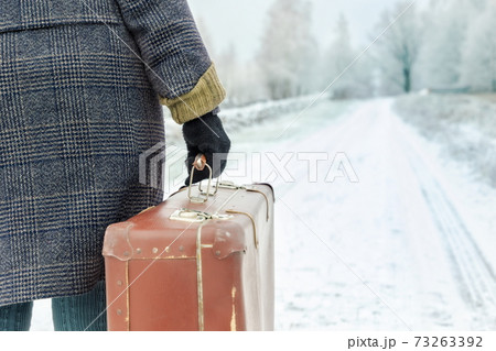 Woman with vintage suitcase walking on road in winter Woman with vintage suitcase walking on road in winter 73263392