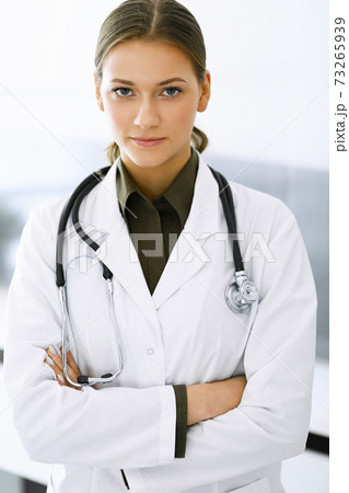 Woman-doctor standing with arms crossed and looking at camera. Perfect medical service in clinic. Medicine and healthcare Woman-doctor standing with arms crossed and looking at camera. Perfect medical service in clinic. Medicine and healthcare 73265939