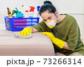 Woman in protective face mask cleaning sofa 73266314