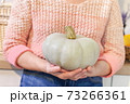 Woman holding green pumpkin in kitchen 73266361