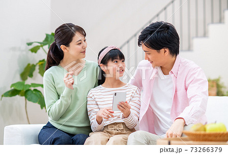リビングでスマホを見る若い家族 73266379