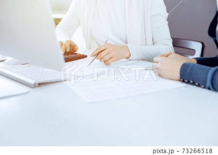 Accountant checking financial statement or counting by calculator income for tax form, hands close-up. Business woman sitting and working with colleague at the desk in office. Audit concept 73266518