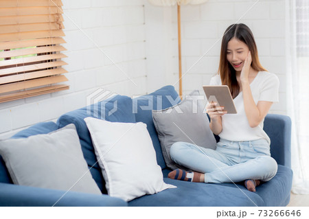 Young attractive asian woman resting using browsing tablet computer on sofa at home. 73266646