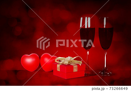 Two wineglasses and red gift box and heart shape on desk with red blur bokeh background. 73266649
