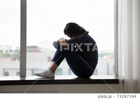 Unhappy hopeless asian woman sitting on windowsill. Unhappy hopeless asian woman sitting on windowsill. 73267184