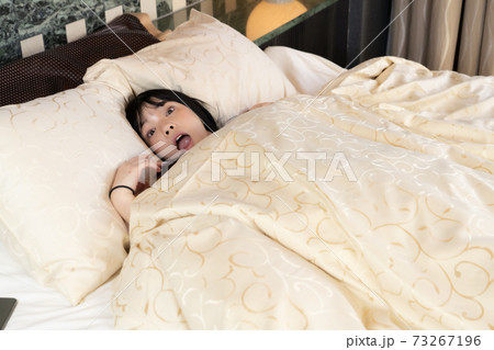 ベッドで寝坊したことに気付いた女性 73267196