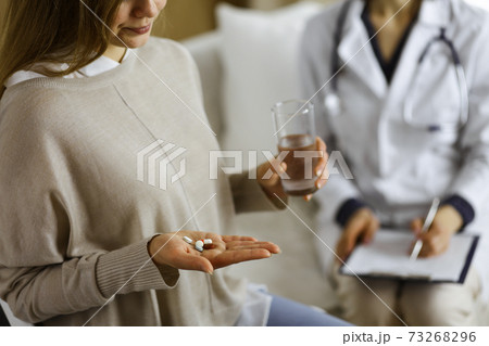 Close-up woman-patient holding pills near her doctor, time to take medications, cure for headache or remedy pain killer drugs. Stay at home concept during Coronavirus pandemic and self isolation 73268296
