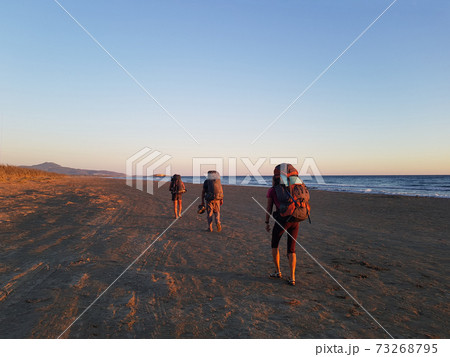 Tourists with backpacks are walking along the beach 73268795