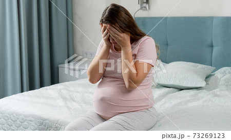 Sad young pregnant woman holding big pillow and sitting on bed. Concept of maternal and pregnancy depression. Sad young pregnant woman holding big pillow and sitting on bed. Concept of maternal and pregnancy depression. 73269123