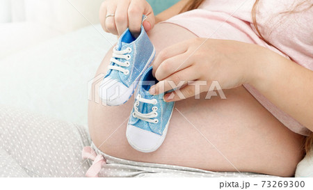 CLoseup of pregnant woman lying in bed and dancing with baby boots on big belly. Concept of pregnancy and expecting baby 73269300