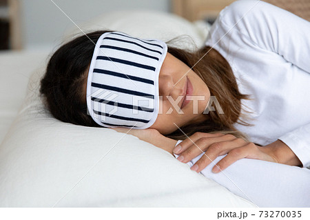 Close up calm woman wearing sleeping mask resting in bed 73270035