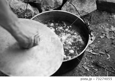 Freshly cooked hot soup in old cauldron on camp fire and man hand with pot cover Freshly cooked hot soup in old cauldron on camp fire and man hand with pot cover 73274055