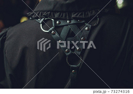 Back shot of a lady with curly hair in a white sleeveless blouse and a black harness made of textile straps with rivets and plastic hooks. The girl is posing. 73274316
