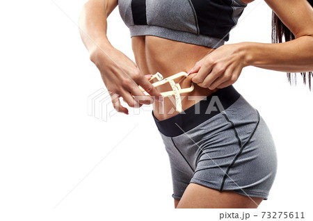 Muscular build fit woman measuring her body fat on abdomen using caliper. Closeup Muscular build fit woman measuring her body fat on abdomen using caliper. Closeup 73275611