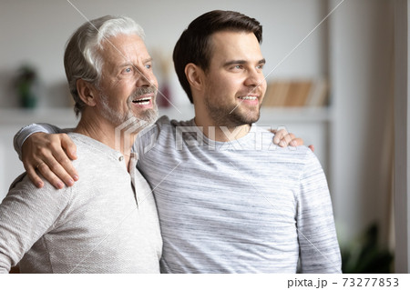 Happy adult son and senior father look in distance Happy adult son and senior father look in distance 73277853