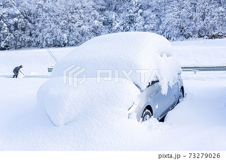 雪にすっぽり埋まった車　雪掻きをする人 73279026