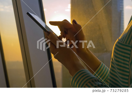 Woman using smartphone against sunset cityscape view through window - close up Woman using smartphone against sunset cityscape view through window - close up 73279285