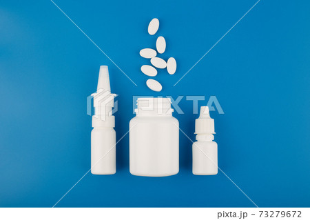 Flat lay with nose spray, medication bottle with spilled pills and eye drops in a row on blue background Flat lay with nose spray, medication bottle with spilled pills and eye drops in a row on blue background 73279672
