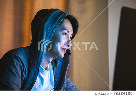 夜にフードをかぶりパソコンをする男性 夜にフードをかぶりパソコンをする男性 73284106