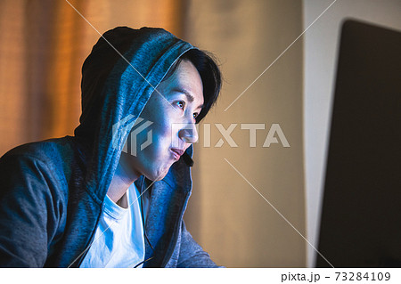 夜にフードをかぶりパソコンをする男性 73284109