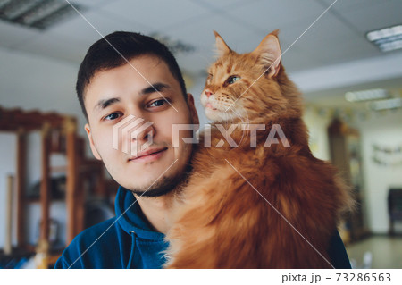 young man holding maine coon ginger cat. young man holding maine coon ginger cat. 73286563