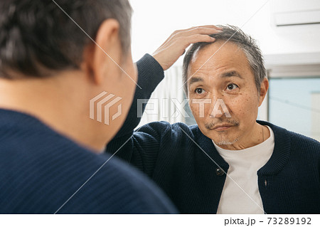 鏡越しにヘアスタイルを見て悩む中高年男性の写真素材