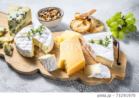 Assorted cheeses on a wooden cutting Board. Camembert, brie, Parmesan and blue cheese with grapes and walnuts. White background. Top view 73291970