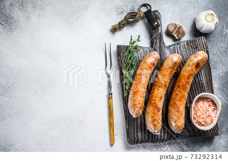 Sausages barbecue fried with spices and herbs on a wooden cutting board. Top view. White background. Copy space Sausages barbecue fried with spices and herbs on a wooden cutting board. Top view. White background. Copy space 73292314