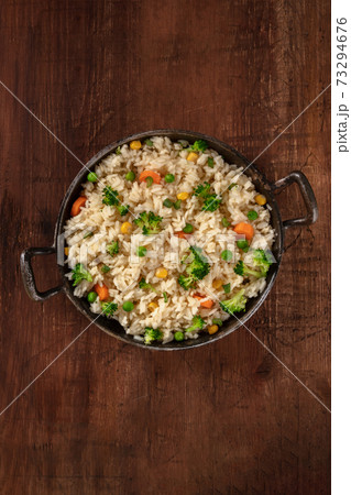 Vegan rice with broccoli, carrots and green peas, shot from above in a frying pan on a dark rustic wooden background Vegan rice with broccoli, carrots and green peas, shot from above in a frying pan on a dark rustic wooden background 73294676