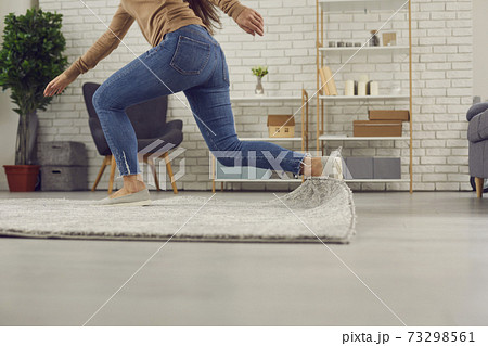 Clumsy woman stumbles on the rug in the living-room and falls down on the floor Clumsy woman stumbles on the rug in the living-room and falls down on the floor 73298561