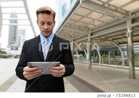 Young handsome blond businessman using digital tablet in the city outdoors Young handsome blond businessman using digital tablet in the city outdoors 73298813