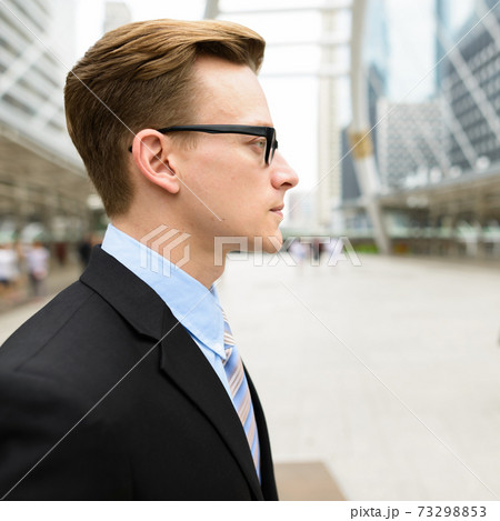 Profile view of young handsome blond businessman with eyeglasses in the city outdoors Profile view of young handsome blond businessman with eyeglasses in the city outdoors 73298853