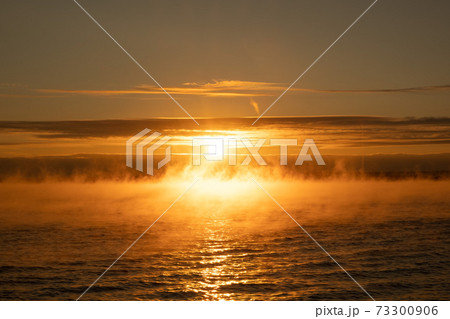 Fog over the sea at sunset. Bright yellow light. The sun against the sky. Water evaporation and heat 73300906