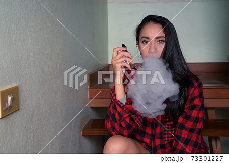 Young beautiful Asian woman vaping at home 73301227