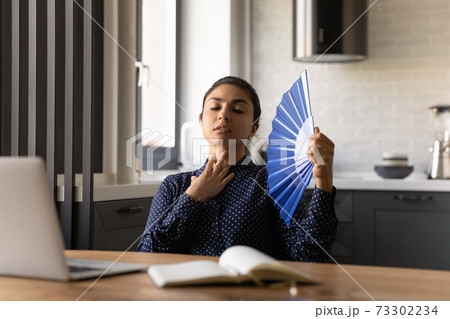 Unwell Indian woman wave with hand fan feeling overheated Unwell Indian woman wave with hand fan feeling overheated 73302234