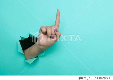 Female hand pointing finger up close-up. Copy space. Torn paper, blue background. 73302654