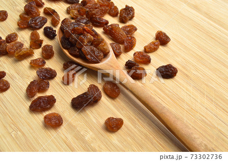 Organic and healthy raisins in spoon on bamboo cutting board 73302736