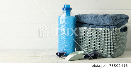 Basket with towels, laundry capsules, scoop with powder and detergent on wooden background Basket with towels, laundry capsules, scoop with powder and detergent on wooden background 73305418