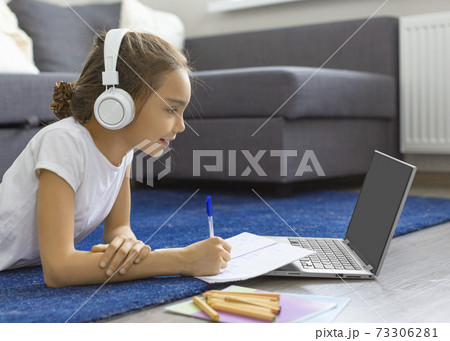 Teenager girl doing her homework online in front of a laptop monitor lying on the floor at home. Teenager girl doing her homework online in front of a laptop monitor lying on the floor at home. 73306281