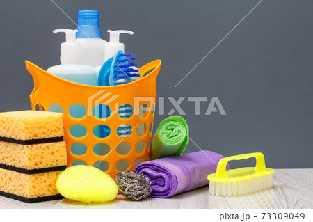 Bottles of dishwashing liquid, brush in a basket and sponges, garbage bags on gray background. Bottles of dishwashing liquid, brush in a basket and sponges, garbage bags on gray background. 73309049