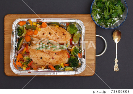 Baked chicken breasts or fillet in metal container with vegetables on cutting board. Baked chicken breasts or fillet in metal container with vegetables on cutting board. 73309303